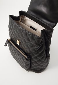 Bolso de mano acolchado de cuero negro con cremallera y cierre dorados, abierto para mostrar un interior de tela beige con un bolsillo interior.