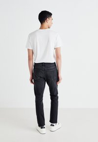 Blugi negri din denim cu o croială slim, prevăzuți cu două buzunare la spate, purtați cu un tricou alb și asortați cu adidași albi.
