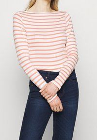 Långärmad topp med båthalsringning, med växlande korall- och vita ränder, kombinerad med mörkblå jeans.