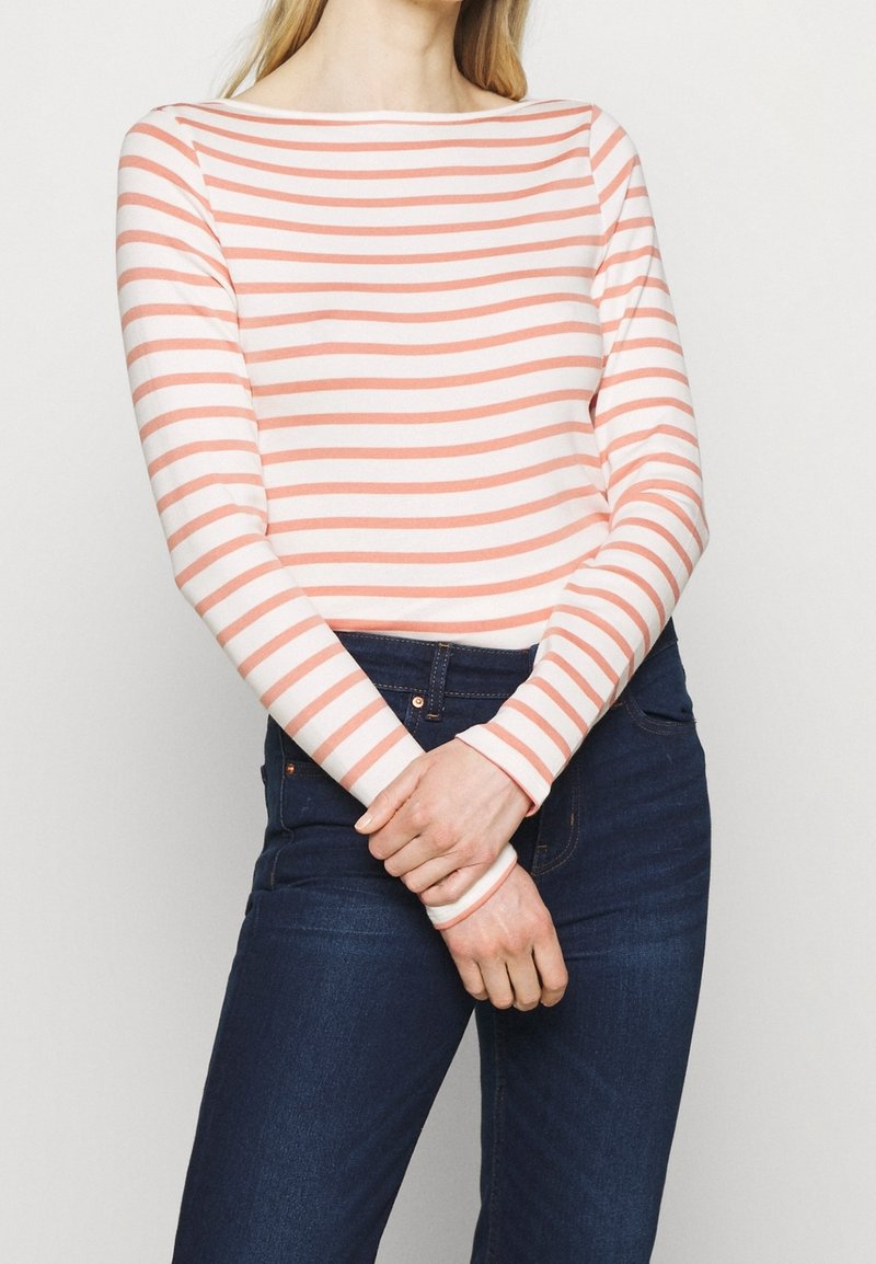 Långärmad topp med båthalsringning, med växlande korall- och vita ränder, kombinerad med mörkblå jeans.