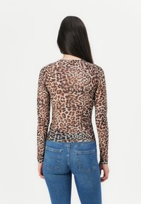 Een leopardprint langemouwen top van doorschijnende stof, met een ronde halslijn en een aansluitend ontwerp, gecombineerd met blauwe spijkerbroeken.