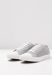 Harmaat verkkokengät valkoisilla kumisilla kärjillä ja nauhoilla. Ominaisuuksina teksturoitu kangas päällinen ja valkoinen, hieman kuviollinen pohja.