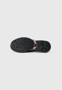 Black rubber outsole with textured grip and a central red accent. Features a patterned tread for traction and stability.