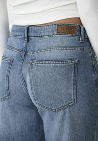 Jeans de mezclilla de color azul claro, con una etiqueta de piel marrón que dice "ONLY" en la cintura, dos bolsillos traseros y detalles de costura visibles.