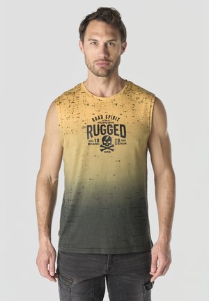 Hombre con camiseta sin mangas de degradado de amarillo a verde oscuro con gráfico de calavera y la palabra "Rugged", y pantalones cargo negros, de pie contra un fondo liso.