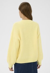 Pull jaune en maille avec une texture côtelée, épaules tombantes et manches larges. Il présente un col rond et un ourlet légèrement court.