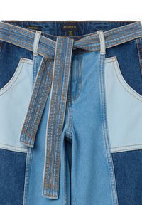 Wijde denim broeken in licht en donkerblauw met een riem. Bevat contrasterende kleuren, gestikte zakken en een zachte textuur.