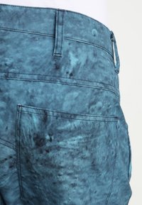 Blue shorts with a textured, marbled fabric. Features a back pocket and belt loops. The material has a slight sheen and varying color depth.