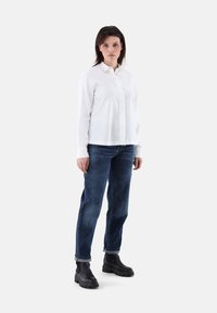 Weißes Hemd mit Knöpfen, blaue Jeans, schwarze klobige Stiefel. Lange Ärmel, strukturierter Stoff, gerade Passform, umgeschlagene Säume, schlichtes Design.
