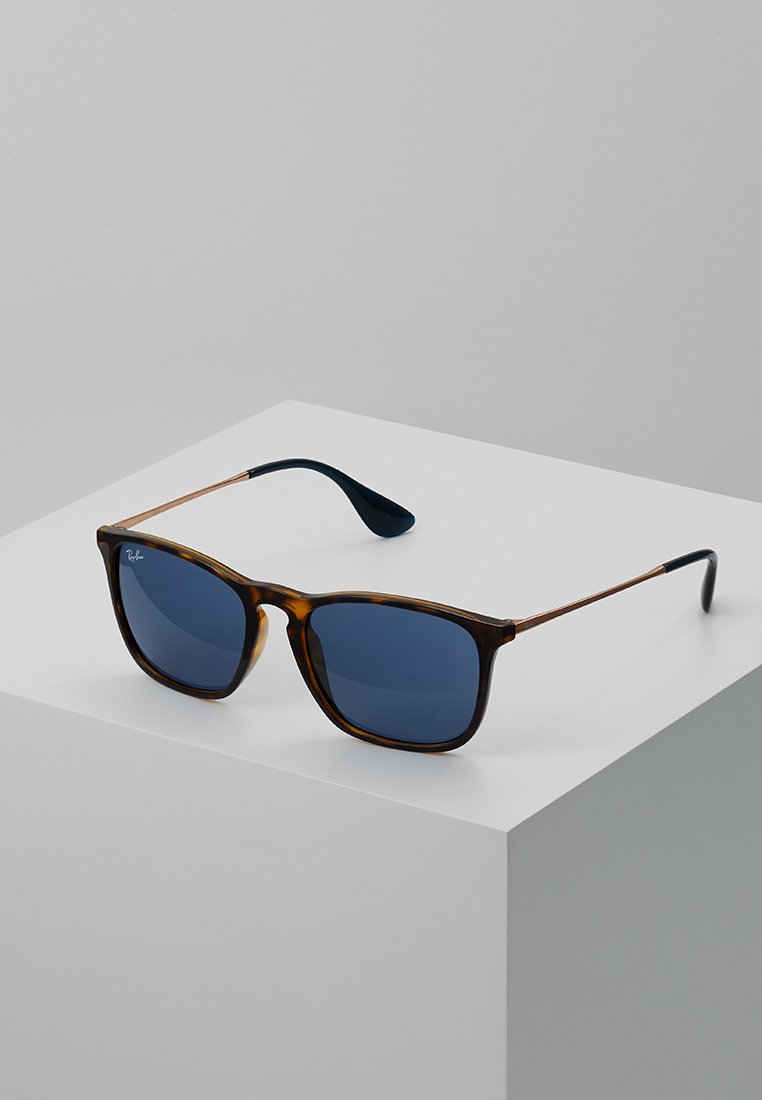 Óculos de sol castanho tartaruga com lentes azul escuras, forma quadrada, armação em metal e plástico, hastes finas com pontas azul escuras.