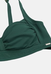 Mørkegrøn tekstureret polstret bikinitop med justerbare stropper og et lille rektangulært metal mærke på siden.