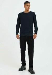 Pull en maille bleu marine avec texture côtelée, col rond et manches longues, associé à un pantalon noir et des bottines noires.