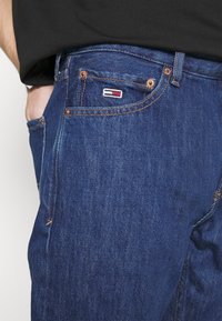 Džínové kalhoty v hluboké indigové barvě s kontrastním šitím. Na přední kapse je malá nášivka s logem a kovové doplňky mají měděnou barvu.