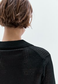 Zwarte gebreide trui met een textuurdesign en een open weefsel, een brede kraag en raglanmouwen, vanaf de achterkant getoond.