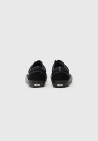 Black low-top sneakers made of suede and canvas, featuring white stitching, rubber sole, and a Vans logo at the heel.