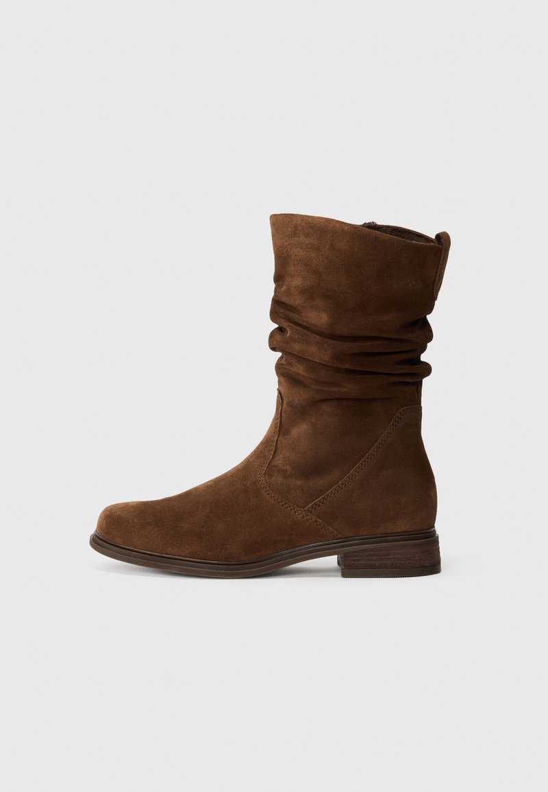Stivaletto in suede marrone con una tomaia morbida, punta rotonda e tacco basso impilato. Il dettaglio di cucitura minimale aggiunge texture.