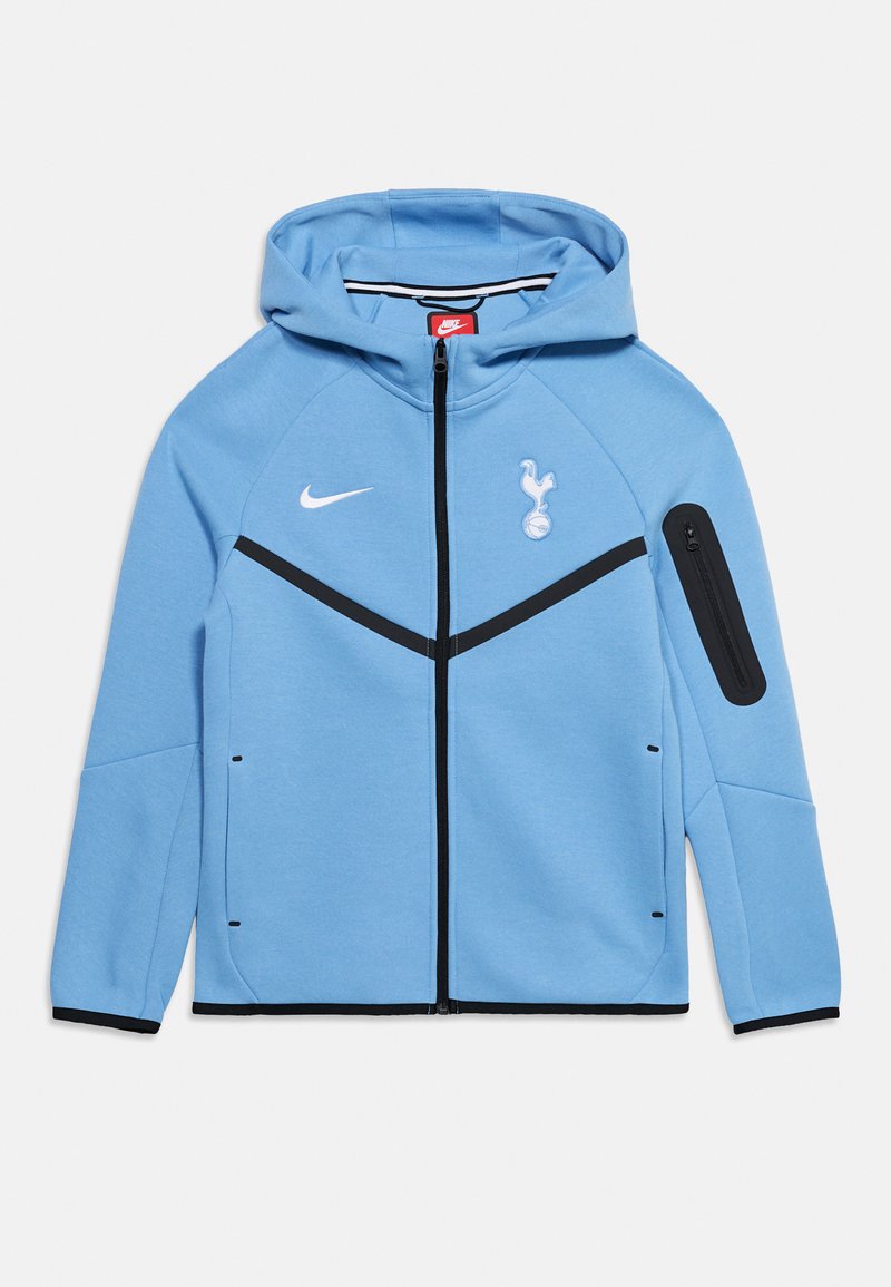 Ανοιχτό μπλε φούτερ με φερμουάρ Nike, μαύρο φερμουάρ, μαύρες λεπτομέρειες, λογότυπο της Tottenham Hotspur στο στήθος και τσεπάκι με φερμουάρ στο αριστερό μανίκι.