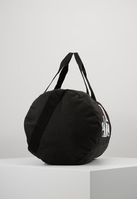 Rund svart duffelbag laget av stoff, med doble håndtak, logodesign og en teksturert overflate. Glatt finish uten synlige dekorasjoner.
