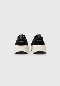 Svart-hvite klumpete sneakers med teksturert overdel, tykk hvit såle og en liten logo på hælen. Har en løfteløkke for enkel bruk.