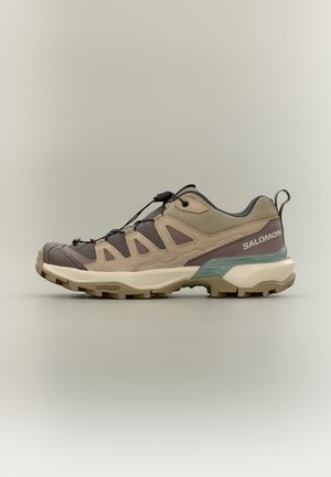 Beige en bruine Salomon wandelschoen met lage snit, meshpanelen, snelvetersysteem, gestructureerde zool en hieltreklip, zijaanzicht.