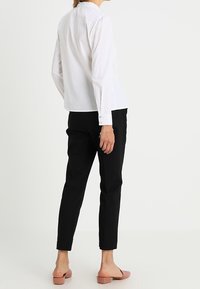 Witte lange mouwen shirt met knopenmanchetten, gedragen met zwarte afgeknotte broek en lichtroze instappers. Eenvoudig ontwerp, geen zichtbare patronen.