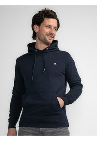 Navyblauer Kapuzenpullover aus Baumwoll-Mischgewebe, mit einer Fronttasche, verstellbaren Kordeln und einem kleinen Logo-Detail auf der Brust.