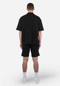 Black short-sleeve shirt with a textured fabric and relaxed fit, paired with matching black shorts. White sneakers and socks complete the outfit.