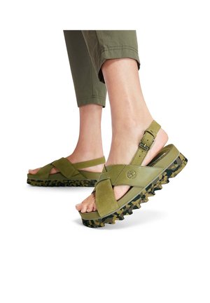 Green suede sandals with crisscross straps, adjustable buckle, and a textured camouflage patterned sole. Casual design suitable for warm weather.