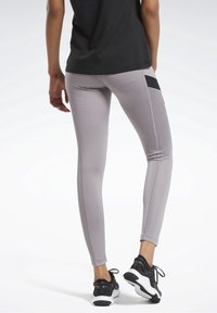 Světle šedé sportovní legíny s žebrovanými bočními panely a černou kapsou, doplněné černobílými běžeckými botami.