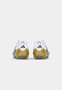 White and black athletic cleats with a glossy yellow sole. Features mesh upper, padded collar, and three black stripes on the side.