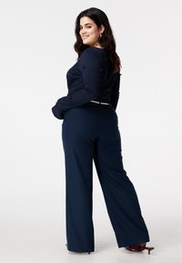 Marineblauwe textuursweater met versieringen, gecombineerd met wijde marineblauwe broekspijpen. Afgewerkt met bordeauxrode schoenen met hoge hak.