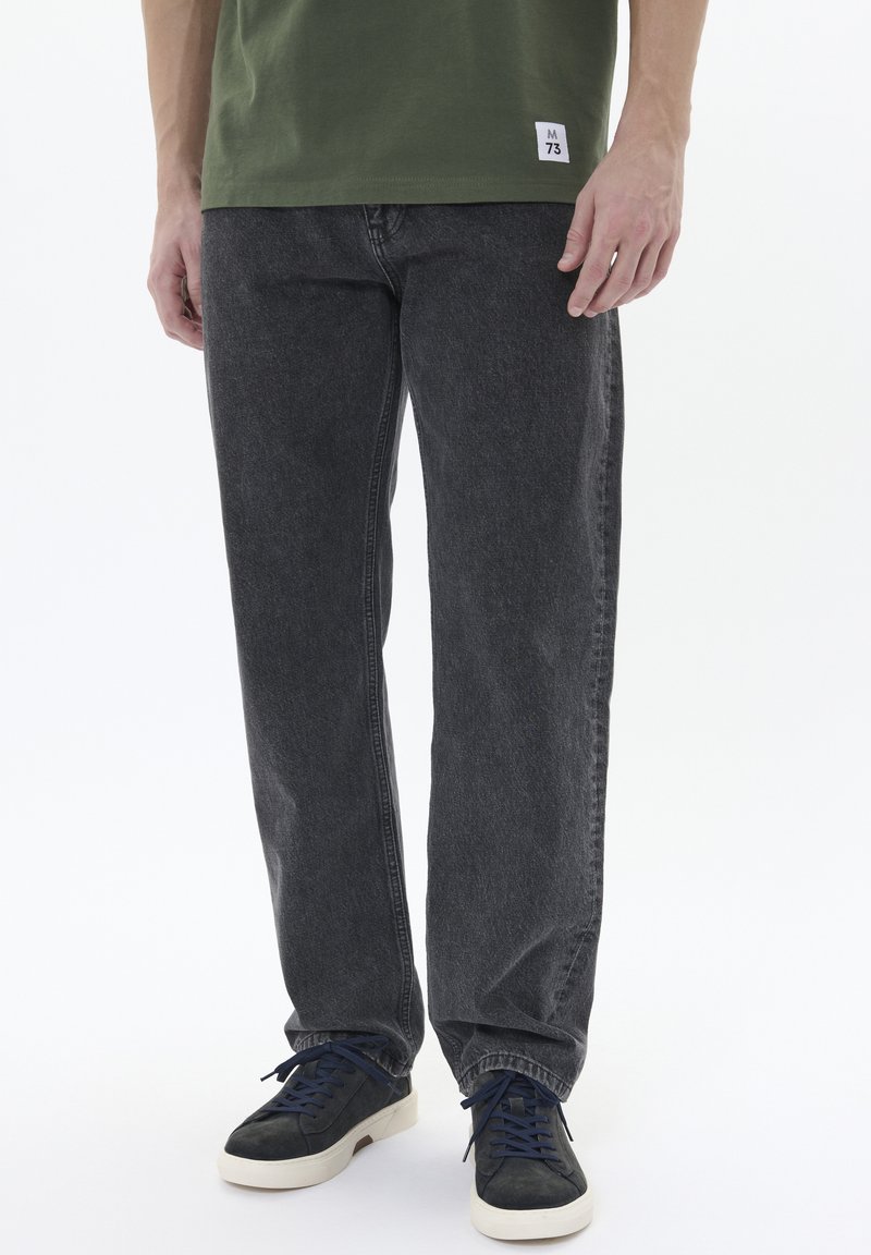 Dunkelgraue gerade geschnittene Jeans aus Denim mit einer leicht abgetragenen Textur, kombiniert mit dunkelblauen Sneakern mit weißen Sohlen.