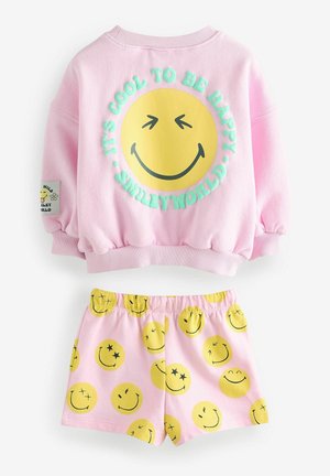 Pink oversized sweatshirt with a large yellow smiley face graphic and text. Matching pink shorts feature various smiley face patterns.
