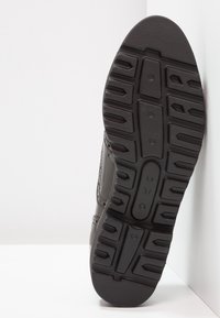 Semelle de sneaker noire avec un motif de traction en caoutchouc texturé. Inclut une marquage de taille '37' et des détails de couture sur le côté.