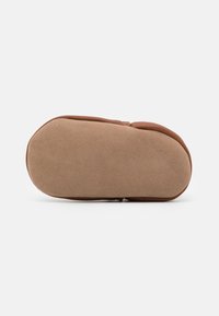 Pantof brown, cu un design simplu în partea superioară și o talpă rotunjită, texturată. Talpa are un design plat, destinat utilizării în interior.
