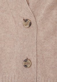 Cardigan beige realizzato in tessuto a maglia fine, con scollatura a V, due grandi bottoni marmorizzati e dettagli a coste lungo i bordi.