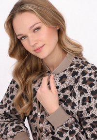 Bomberjacke mit Leopardenmuster in Beige, Braun und Schwarz. Verfügt über einen Reißverschluss und gerippte Bündchen, die einen lässigen Schnitt und eine weiche Textur hervorheben.