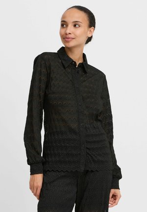 Black semi-transparent shirt with a textured pattern, long sleeves, and a button-up front. Features a pointed collar and fitted cuffs.
