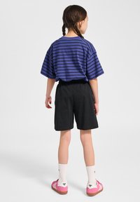 Lila och svart randig t-shirt med korta ärmar, svarta shorts, rosa skor och vita strumpor, sedd bakifrån. Enkel design och avslappnad passform.