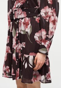 Σκοτεινό λουλουδάτο φόρεμα με ρόζ και λευκά λουλούδια, μπροστινό μέρος με κουμπιά, ζώνη στη μέση και μακριά μανίκια με μανσέτες με κουμπιά.