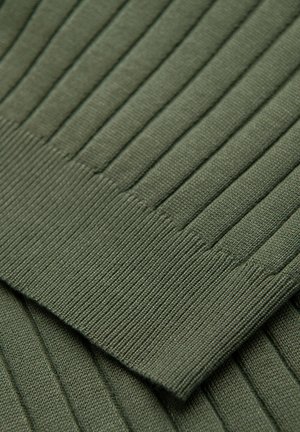 Gros plan d'un tissu en maille côtelée vert foncé montrant la texture détaillée et les coutures d'une manche de vêtement pliée.