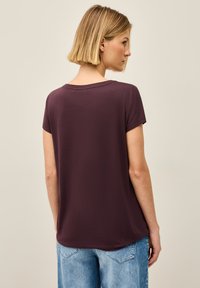 Bordeaux kortærmet bluse med en afslappet pasform og rund halsudskæring. Blødt materiale, lige kant og subtil detalje med søm bagpå. Kombineret med denimjeans.