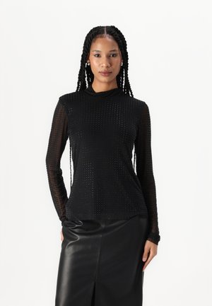 Maglietta nera a maniche lunghe con un design aderente, caratterizzata da un motivo a pois testurizzato e un collo alto, abbinata a una gonna di pelle nera a vita alta.