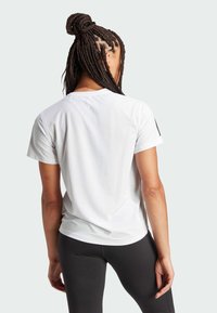 Fehér, rövid ujjú sport póló kerek nyakkal, sima textúrával és fekete részletekkel az ujjakon. Fekete, testhez simuló leggings-szel párosítva.