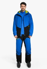 Blauer wasserdichter Anorak und Hose mit schwarzen Akzenten. Die Jacke hat eine grün gefütterte Kapuze und Reißverschlusstaschen. Strukturierter Stoff, normale Passform.