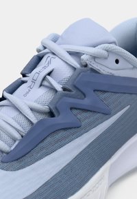 Sapatilha atlética azul clara com material em malha, acentos em zigzag, tecido texturizado e um design elegante com elementos brancos e azul escuro.