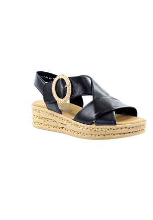 Sandalia negra de cuero con suela de plataforma beige, correas cruzadas y hebilla grande y redonda beige en la correa del tobillo.