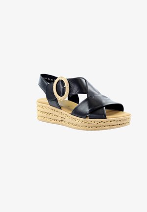 Sandalia negra de cuero con suela de plataforma beige, correas cruzadas y hebilla grande y redonda beige en la correa del tobillo.