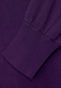 Närbild av en lila stickad tröjsleeve med en ribbad mudd och detaljerad sömnad på en strukturerad tygbakgrund.