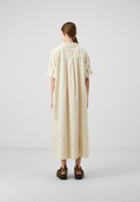 Abito maxi fluido color beige chiaro con maniche a palloncino corte e colletto con bottoni, caratterizzato da una piega posteriore per maggiore volume.